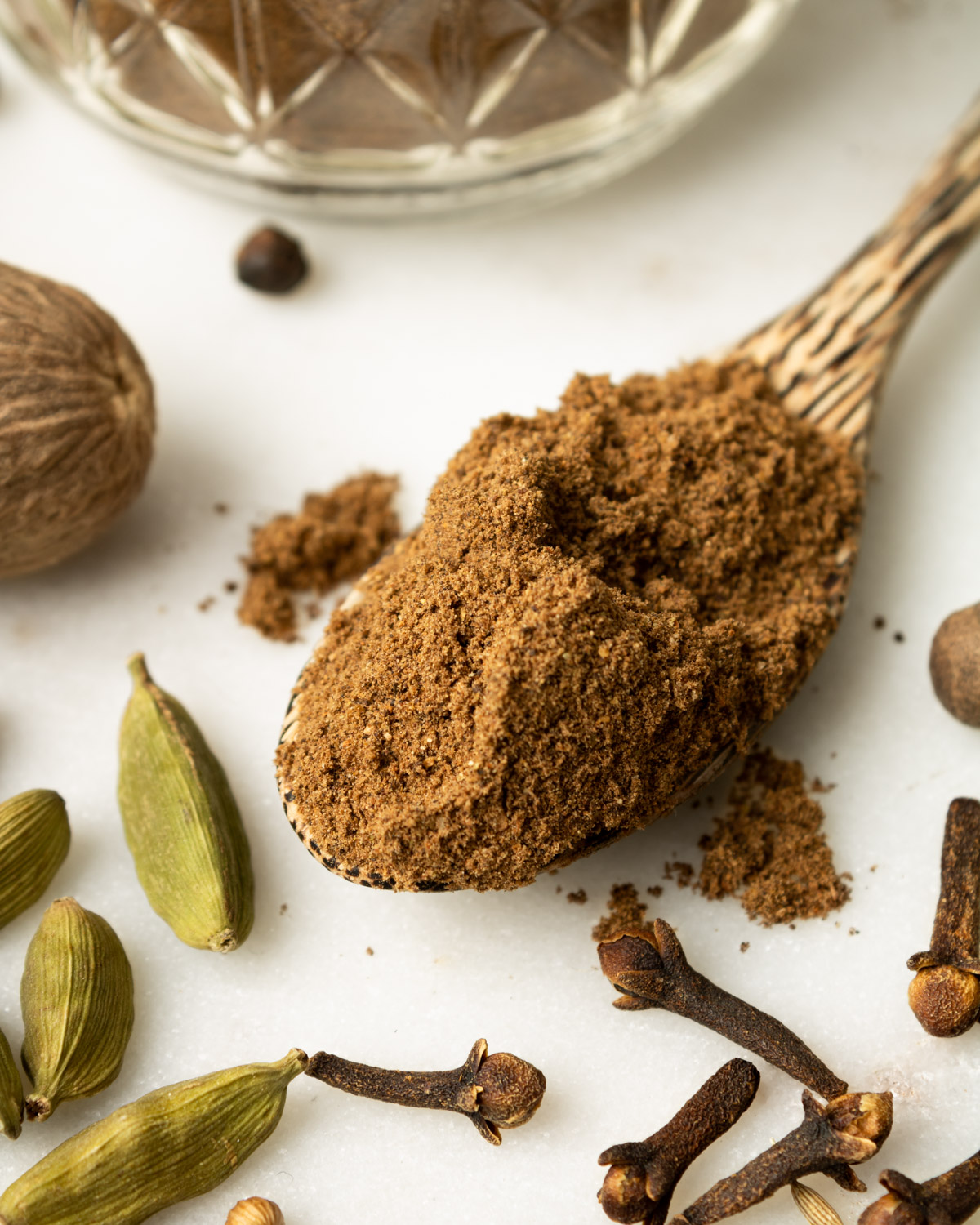 close up of a spoonfull of Lebanese seven spice on a white counter surrounded with whole spices.