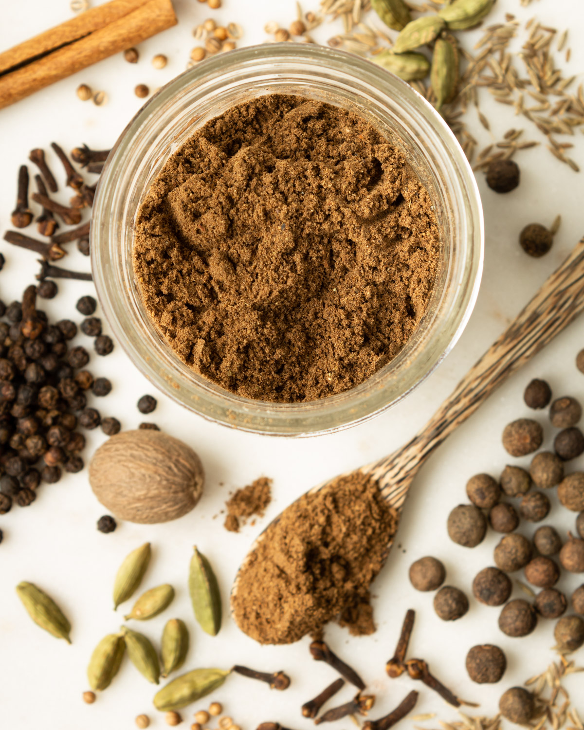 Lebanese seven spice in a glass jar on a counter full of whole spices.