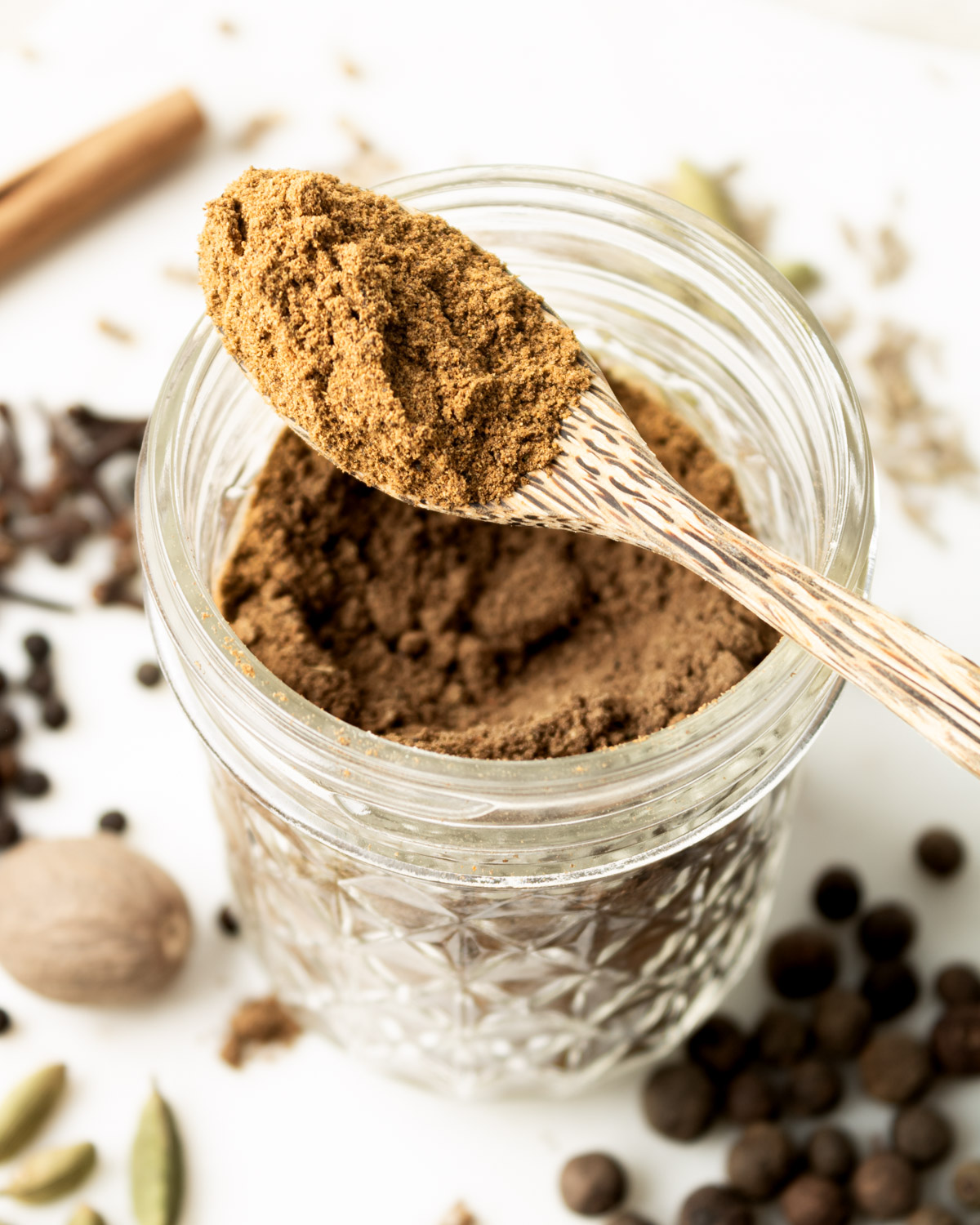 a spoonful of baharat sitting on the edges of a glass jar.