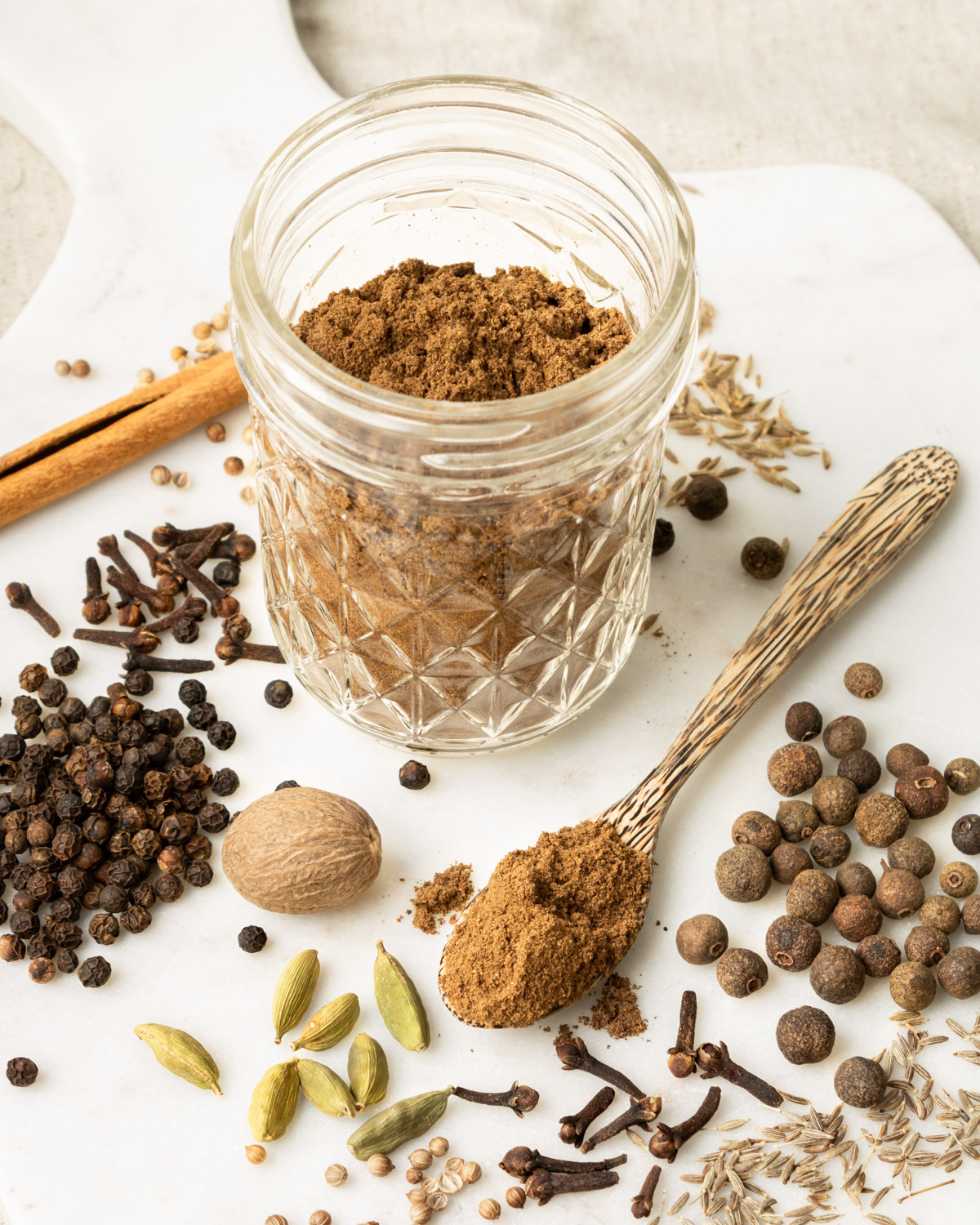 a glass jar with ground Lebanese 7 spice surrounded with different whole spices.