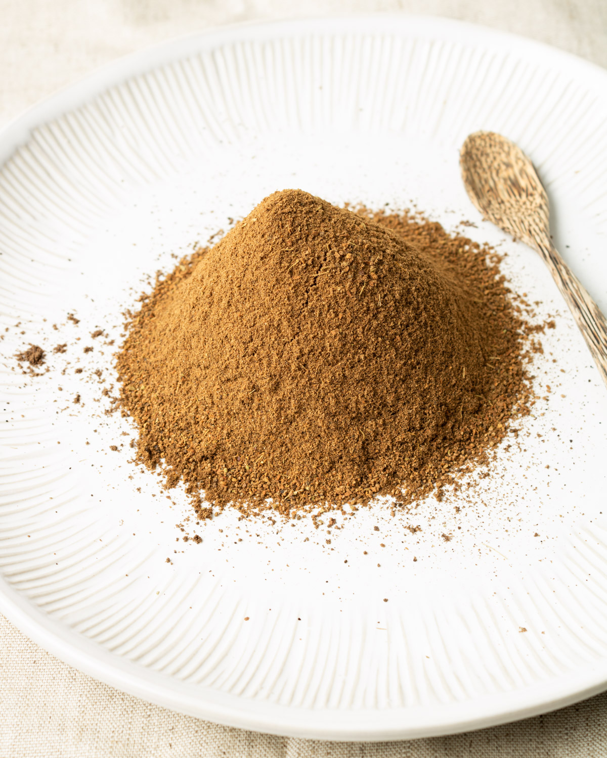 ground Lebanese seven spice blend on a white plate with a wooden spoon.