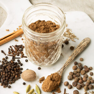 a glass jar with ground Lebanese 7 spice surrounded with different whole spices.